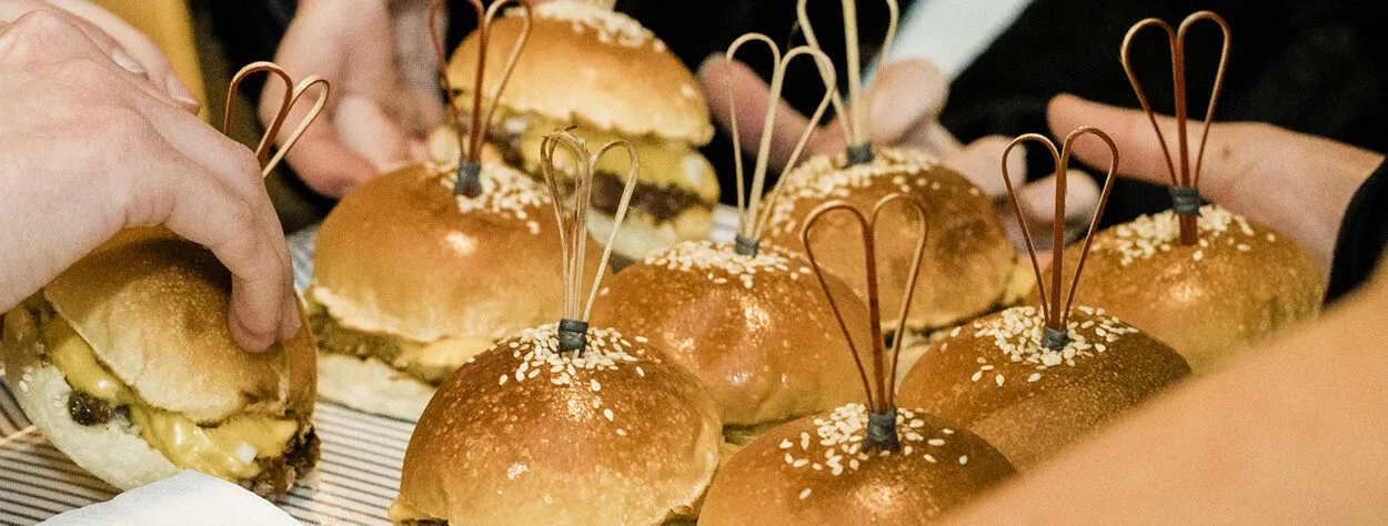 2 Guests are grabbing cheeseburger sliders off a platter being passed around by wait staff. 